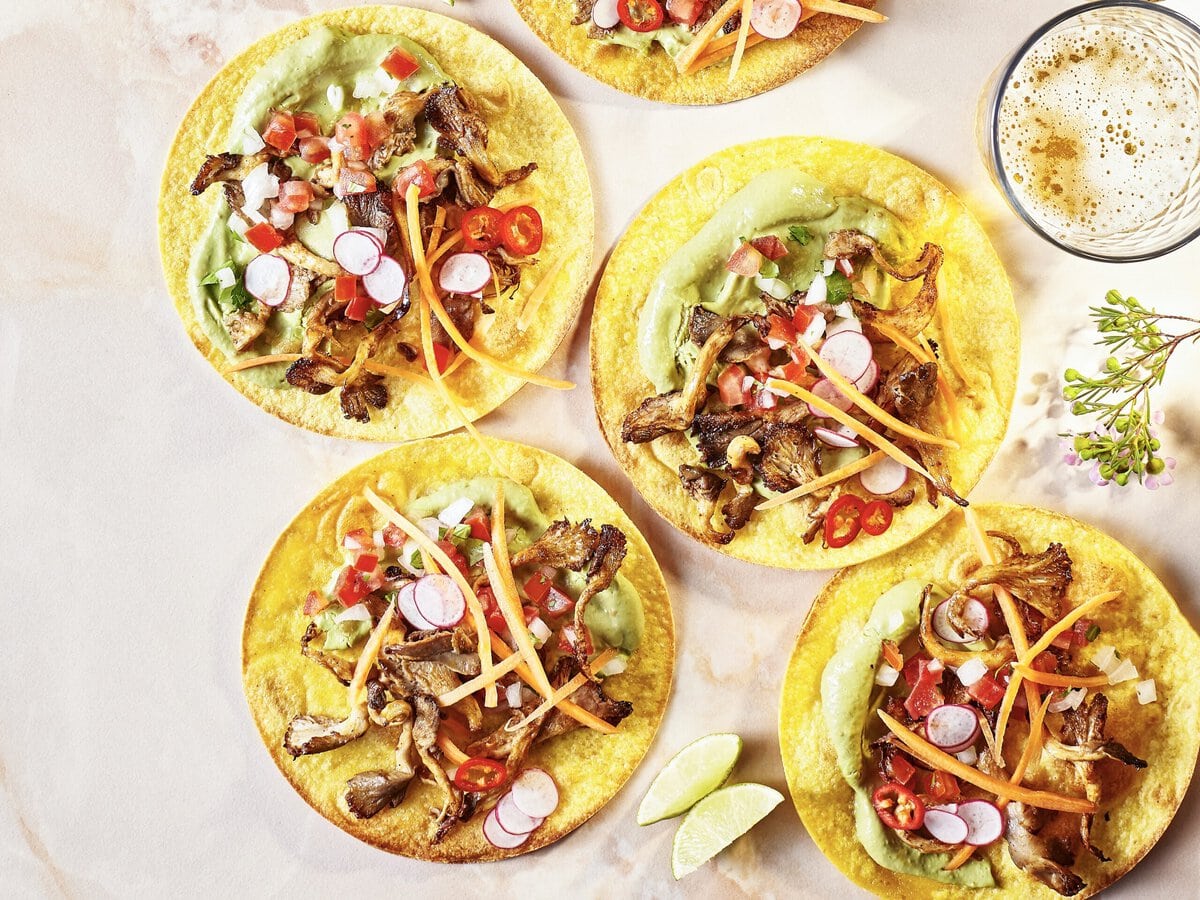 4 tostada’s met onder andere pulled oesterzwam, avocadocrème, rode peper en radijs, geserveerd met limoenpartjes