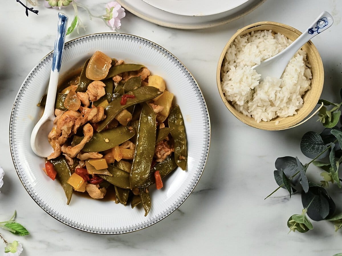 Bakje zoetzure kip met sugar snaps, paprika en ui, met daarnaast een bakje rijst