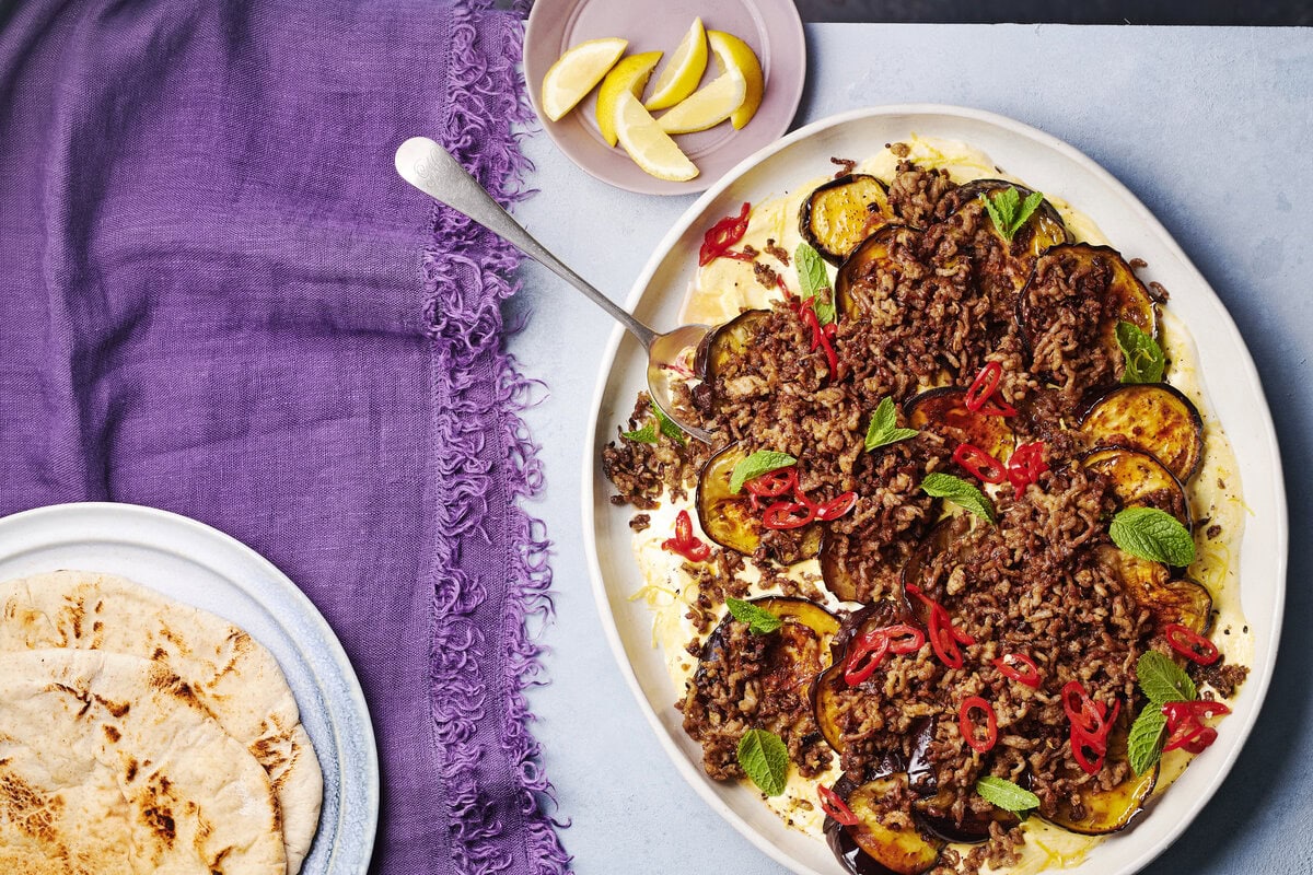Geroosterde aubergine met daarop rul lamsvlees, rode peper en munt, geserveerd met flatbread en partjes citroen