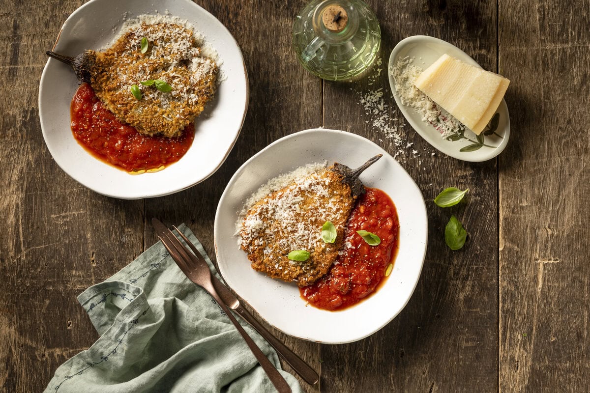 Twee borden aubergineschnitzels met Parmigiano Reggiano erover, geserveerd met tomatensaus