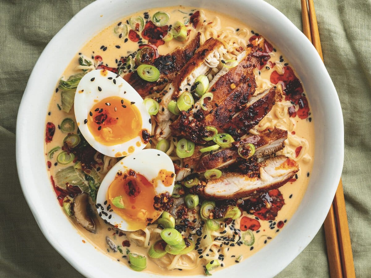 Noedels in een creamy bouillon met kip, een zachtgekookt ei, lente-ui, zwart sesamzaad en crispy chili-olie