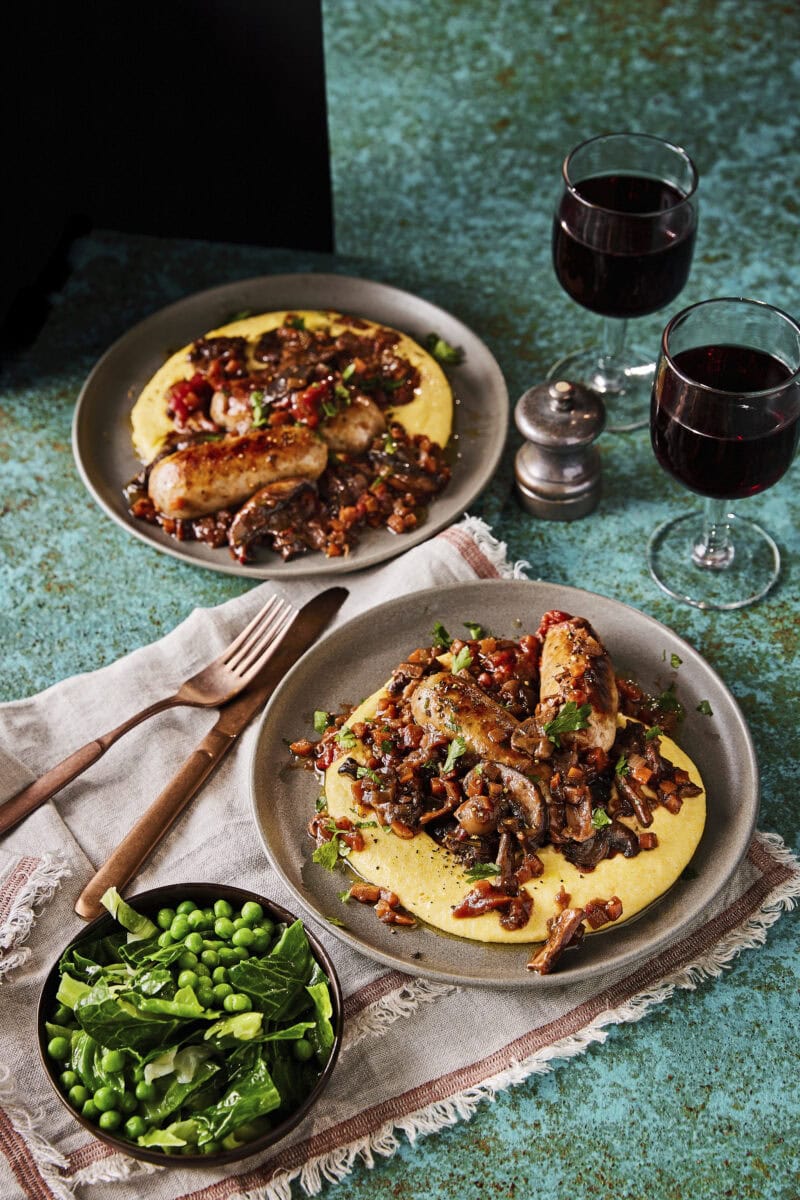 Twee borden gestoofde Italiaanse worstjes met champignons, romige polenta en gestoomde groene groenten