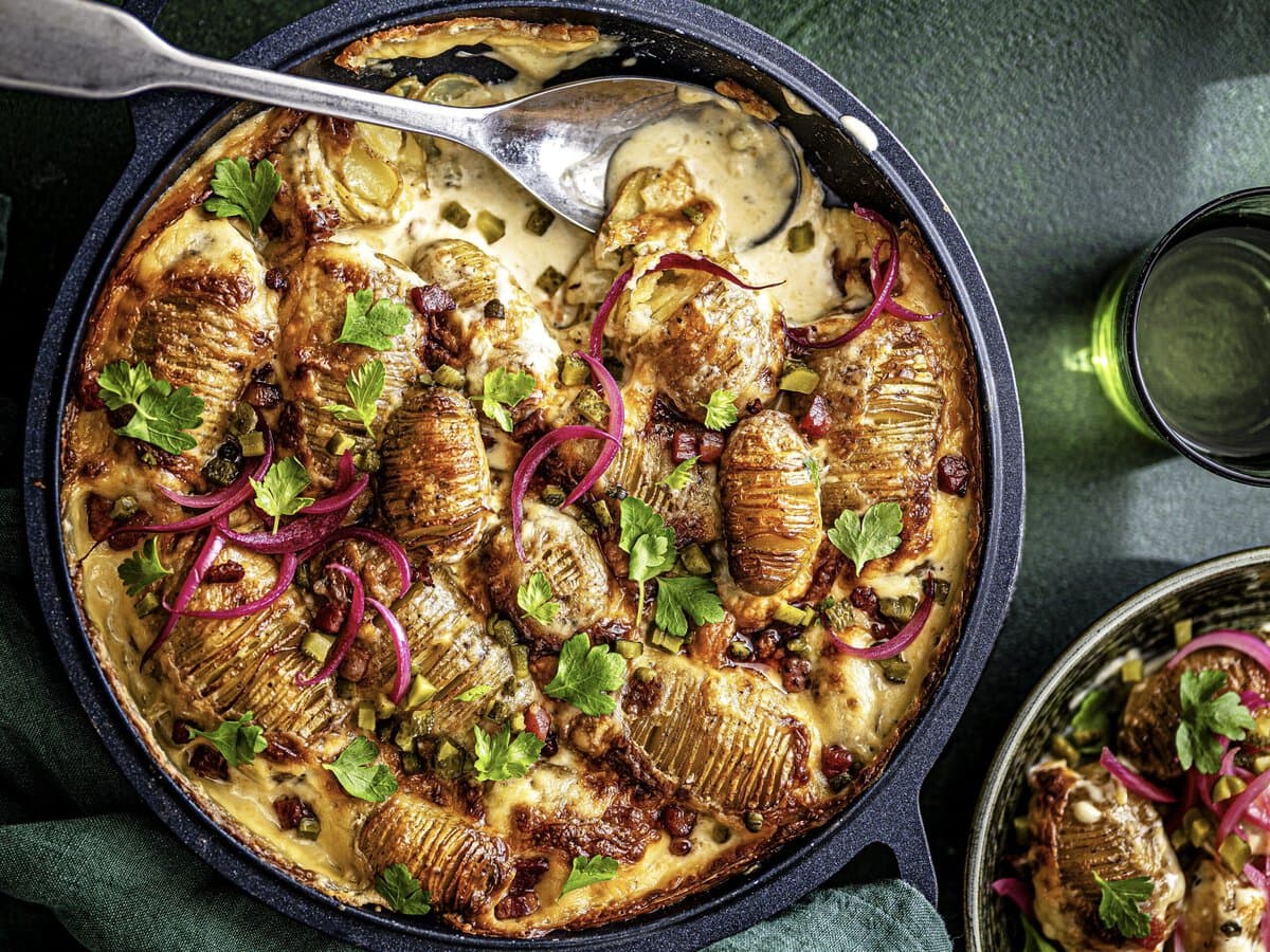 Tartiflette met hasselback aardappelen, peterselie en ingelegde rode ui, geserveerd met picklesalade