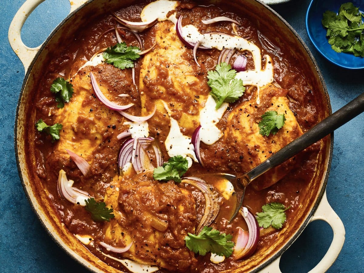 Heilbot met rokerige masalasaus in een pan met rode ui, koriander en yoghurt