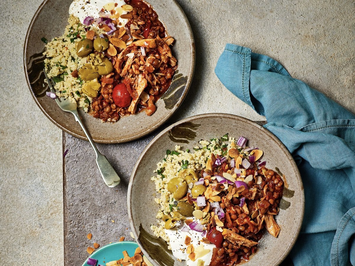 Twee bowls met harissa pulled chicken, couscous, yoghurt, olijven, rode ui en amandelschaafsel