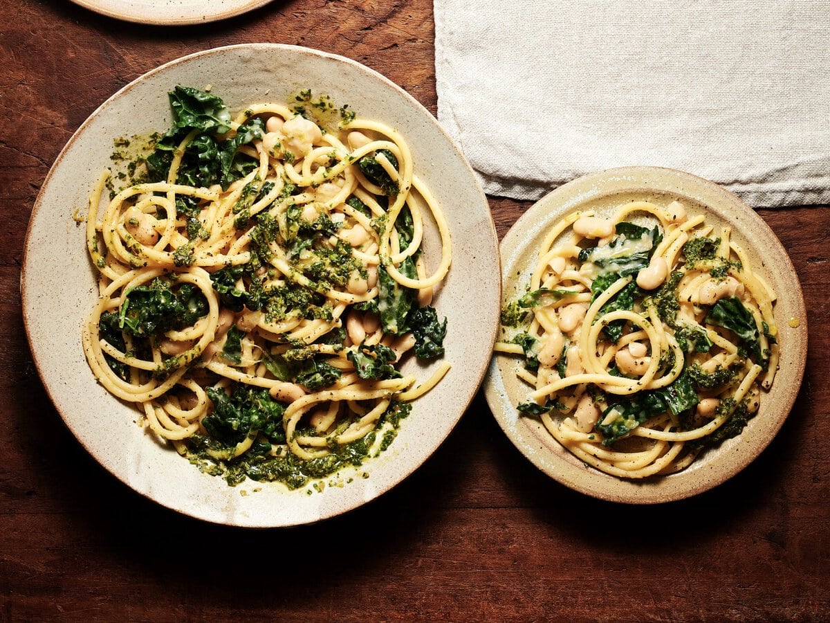 Twee borden romige pasta met bonen en boerenkool met daarover salsa verde