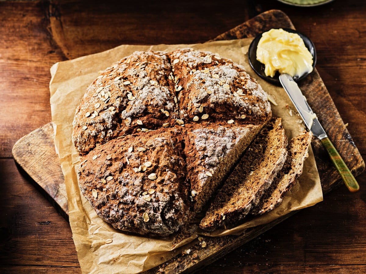 Donker brood met bovenop een kruis en havervlokken, geserveerd met boter