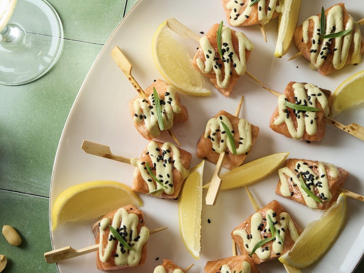 Warmgerookte-zalmspiesjes met dragonmayonaise en zwart sesamzaad erover, geserveerd met partjes citroen