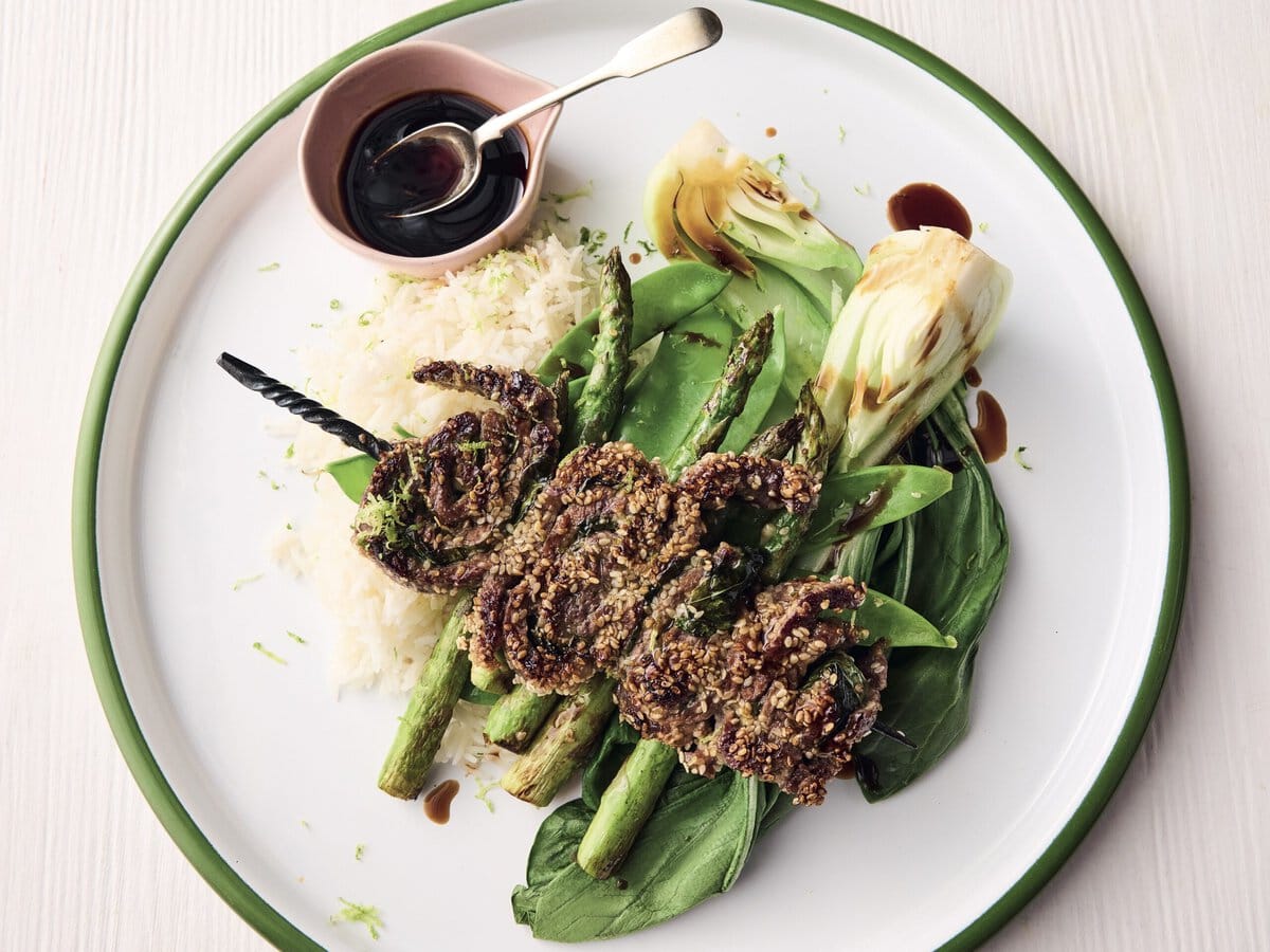 Steakspiesjes met wasabi en sesamzaad, geserveerd op rijst, paksoi, groene asperges en met een bakje teriyakisaus