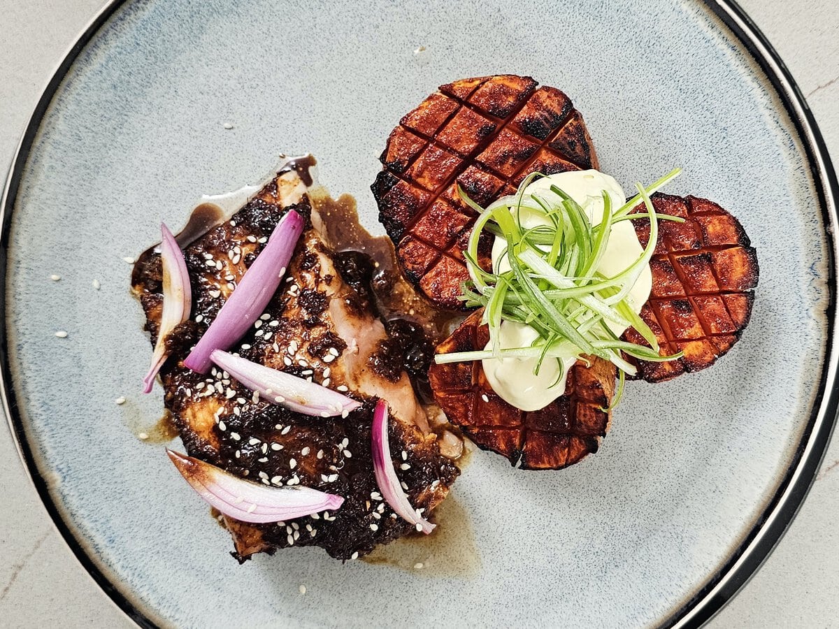 Zalm in marinade met daarop wit sesamzaad en rode ui, geserveerd met zoeteaardappelmedaillons met daarop mayonaise en lente-ui