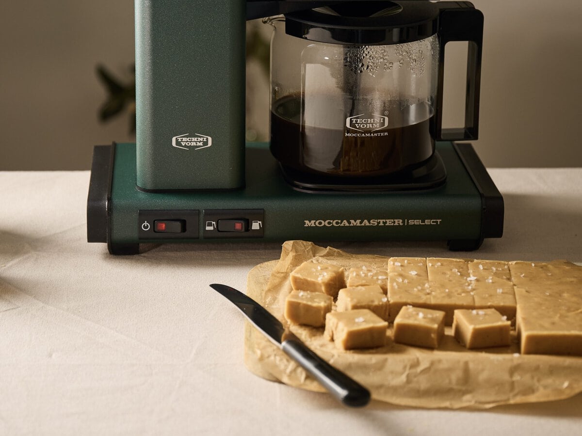 Fudge met miso en koffie en zeezout erover in blokjes gesneden met op de achtergrond een filterkoffiezetapparaat